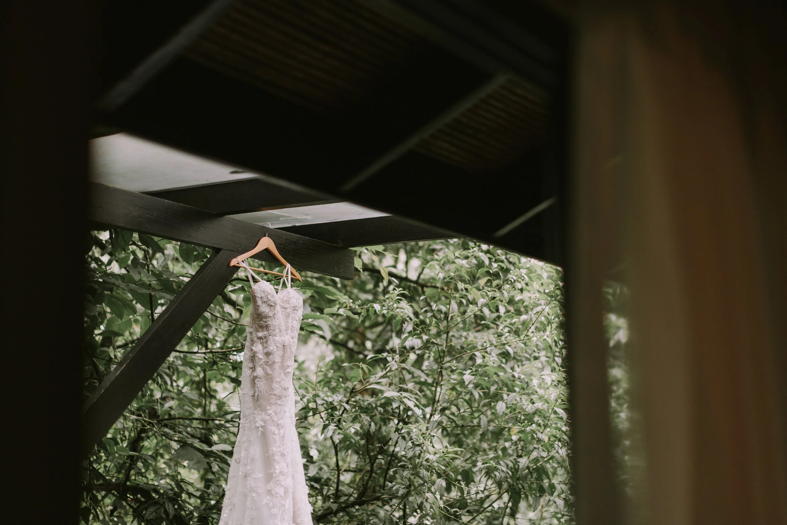 Lace wedding gown hanging from a dark beam over the rainforest canopy in Costa Rica