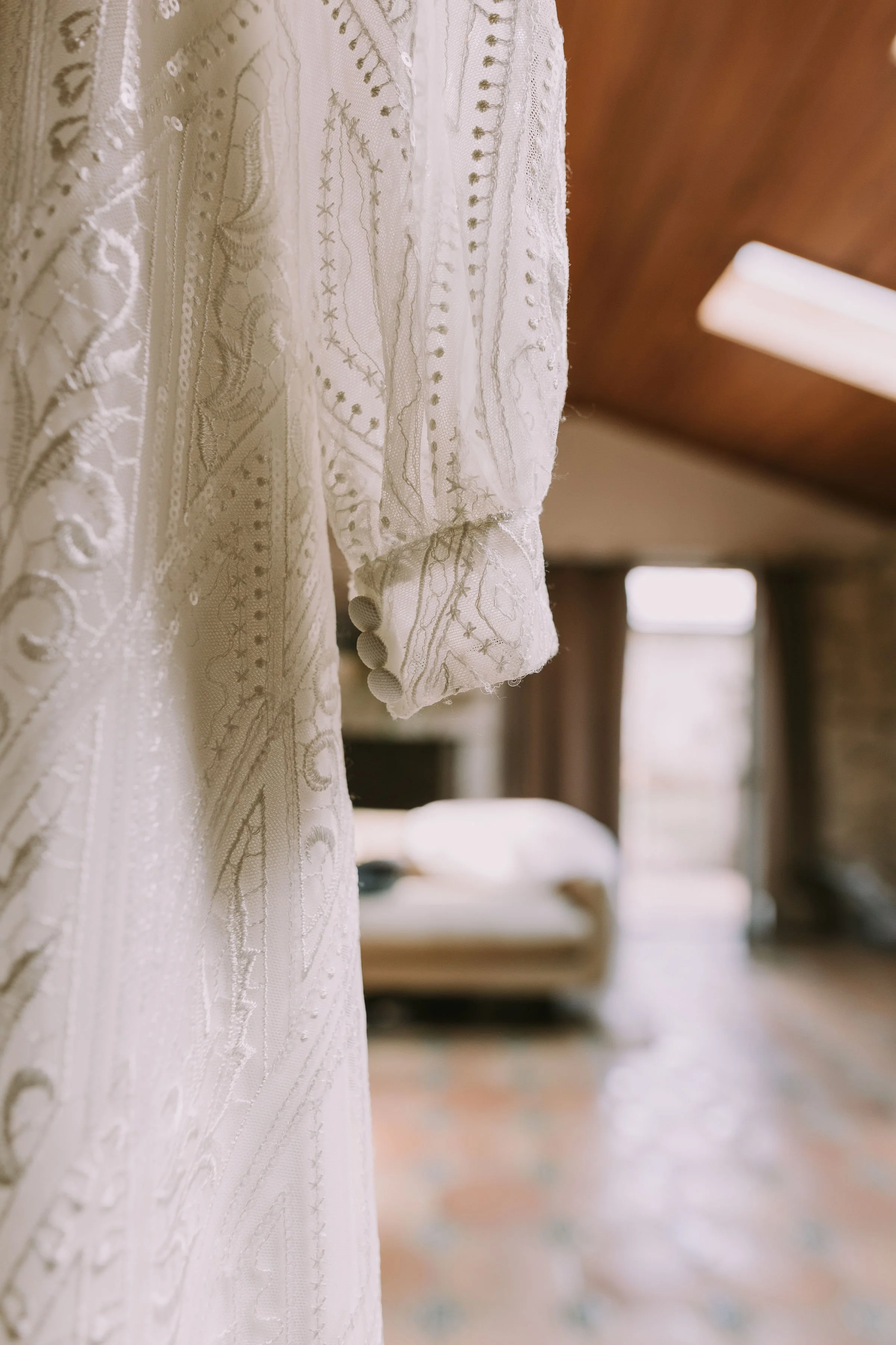 Lace sleeve of a wedding dress hanging in a stone getting-ready suite with a vaulted wood ceiling in Wimberley, Texas