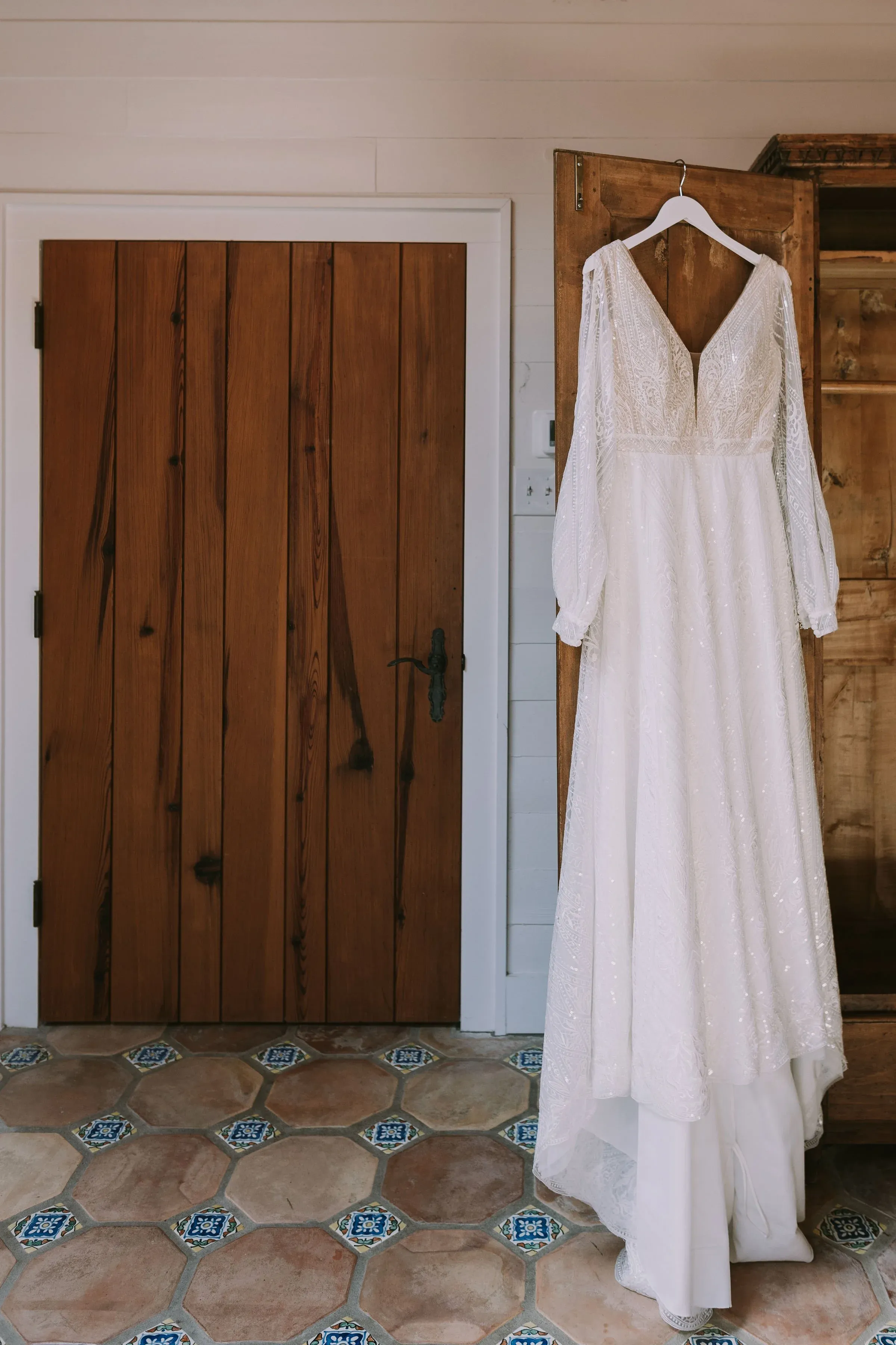 Beaded long sleeve gown hung on a wardrobe door above painted Saltillo tile in Wimberley, Texas