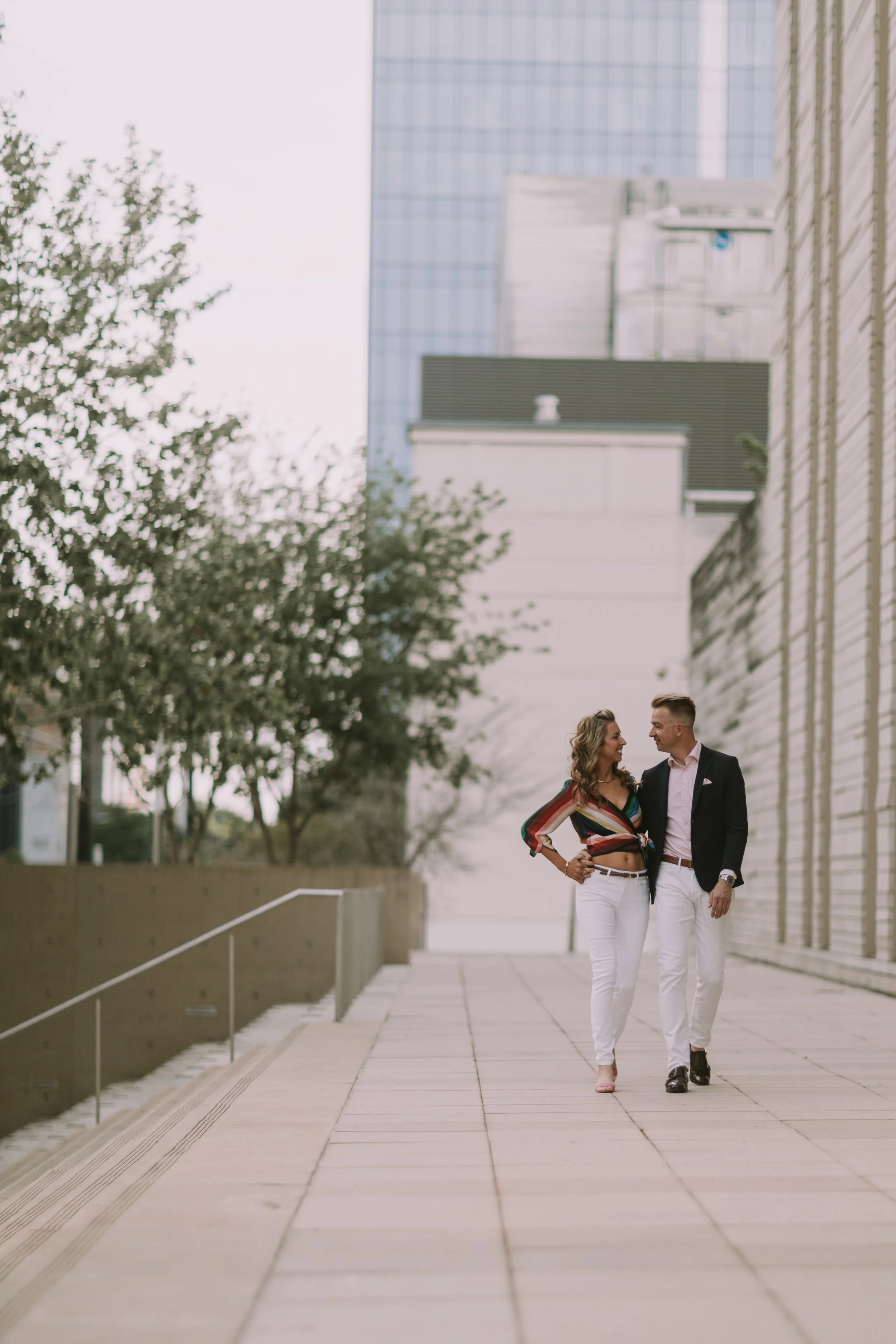 Mathias and Doralicia walking arm in arm down a modern walkway between Austin high-rises