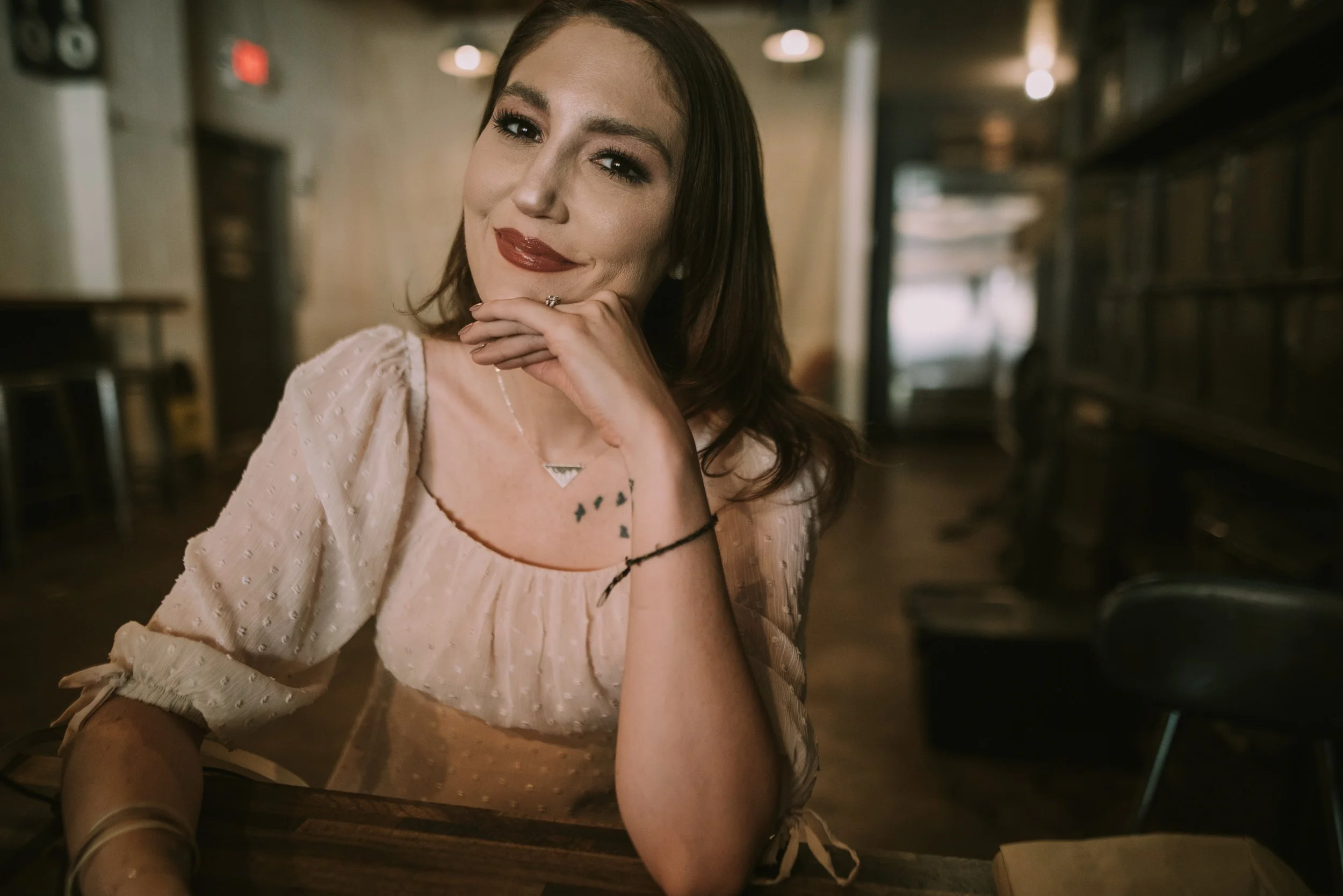 Molly rests her chin on her hand in a warm-lit Austin bar during her engagement session