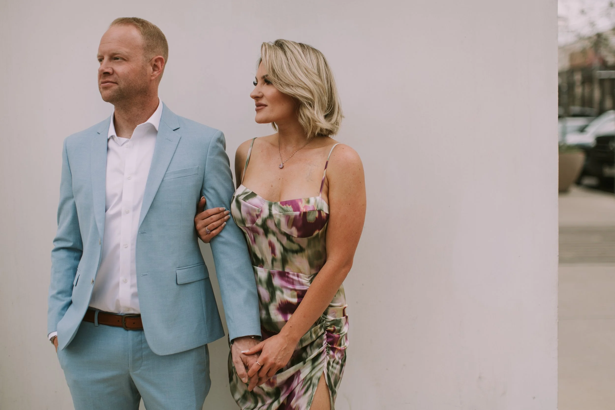 Ryan and Tessa arm in arm against a white wall, both looking off frame, during a couples session in Austin, Texas