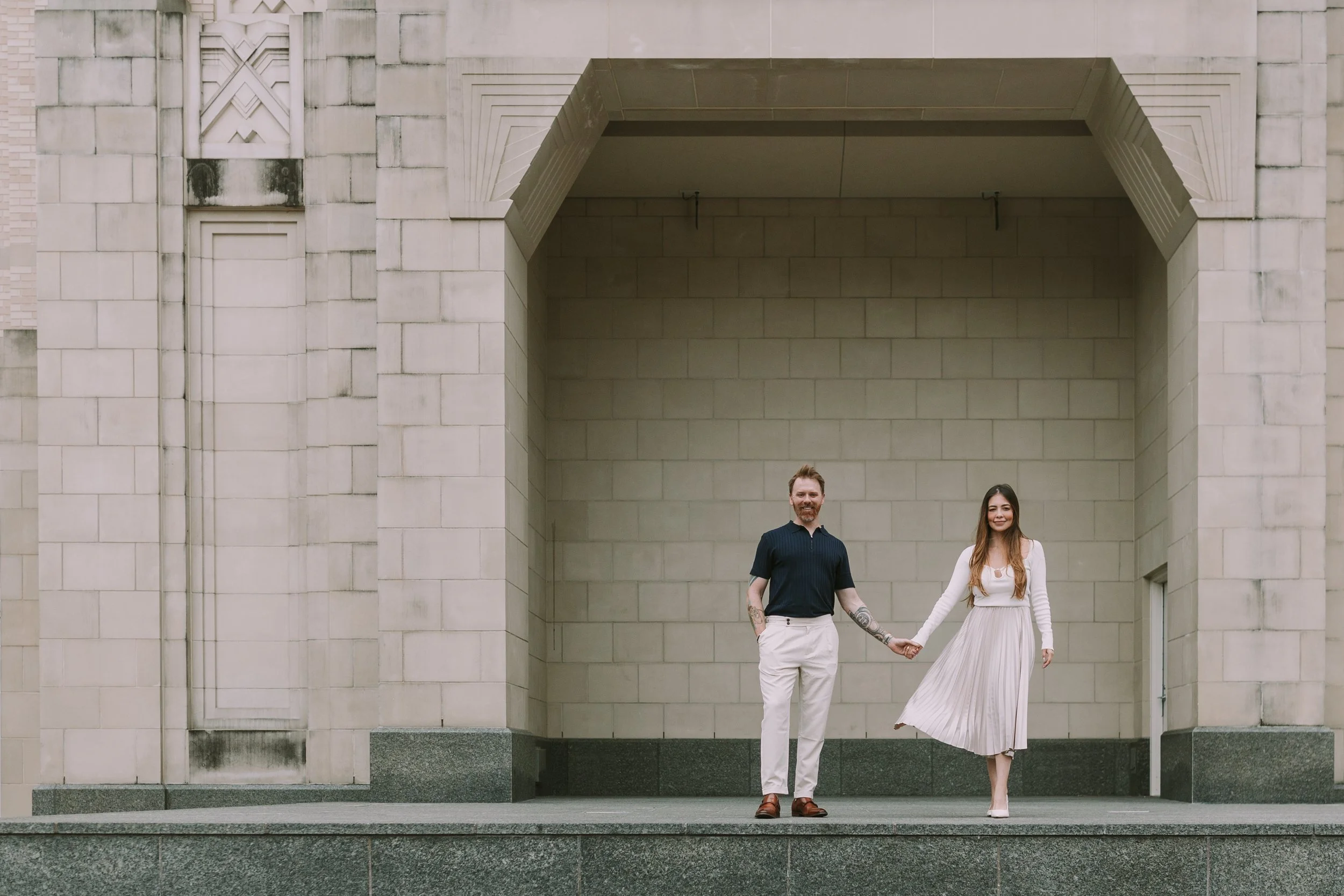 Sean and Maria holding hands beneath a carved limestone archway in downtown Fort Worth